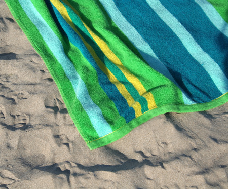A green, blue and yellow beach towel sitting in the sand.の写真素材
