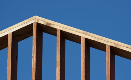 The crest of the wooden frame of a new house set against the blue sky.