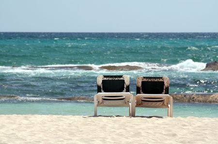 Two unoccupied beach chairs facing out onto the Caribbean sea.