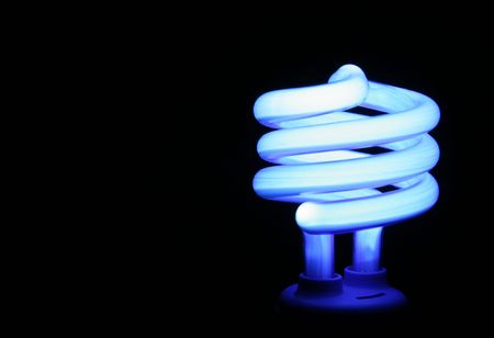 A blue compact flourescent energy saver light bulb set against a black background.の写真素材