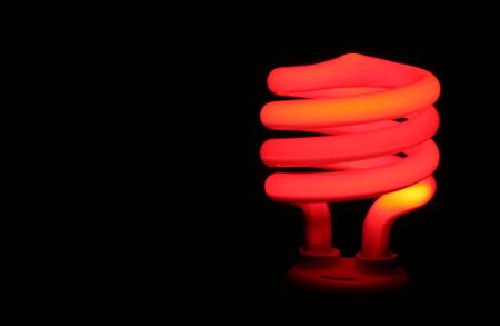 A red compact flourescent energy saver light bulb set against a black background.の写真素材