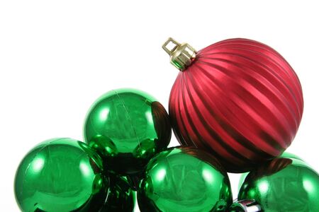 A red bauble sitting on a bunch of green Christmas baubles against a white background.の写真素材