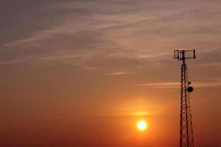 The silhouette of a cell phone tower shot against the orange cast of the setting sun.の写真素材
