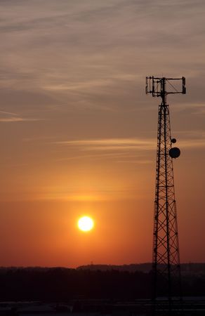 The silhouette of a cell phone tower shot against the orange cast of the setting sun.の写真素材