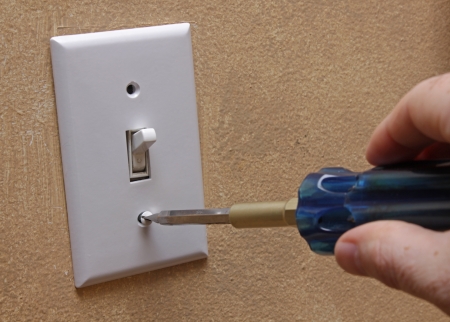 A hand using a screw driver to screw in a light switch cover.の写真素材