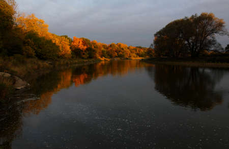The sunrising on the autumn coloredd trees lining the Grand River. Shot in Waterloo, Ontario, Canada.の写真素材