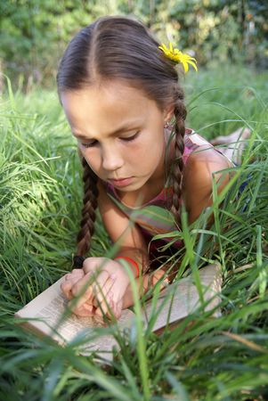 Preteen girl reading book on green grass backgroundの写真素材