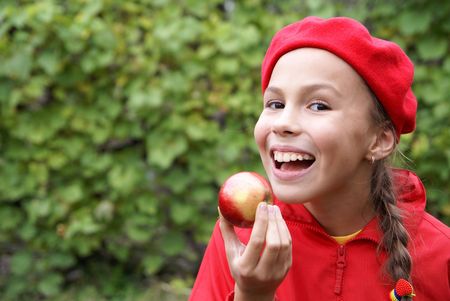 Cheerful preteen girl eats apple on green leaf backgroundの写真素材