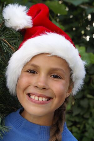 Smiling preteen girl in Santa's red hat on pine tree backgroundの写真素材