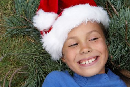 Smiling preteen girl in Santa's red hat on pine tree backgroundの写真素材