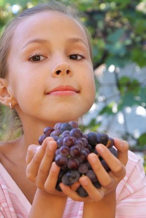 Smiling preteen girl with grapes on grapevine backgroundの写真素材