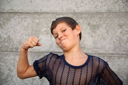 Preteen boy showing big muscles outdoors              