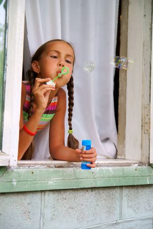 Preteen girl blows bubbles sitting in windowの写真素材