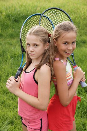 Happy preteen girls in sport outfits with tennis rackets on green grass backgroundの写真素材