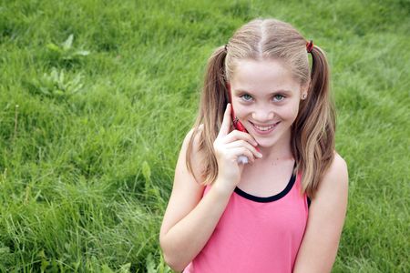 Happy teenage girl talks on ceellural phone on green grass backgroundの写真素材