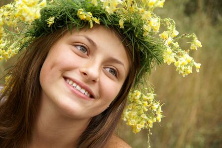 Beautiful cheerful teenage girl in field flower garland outdoorsの写真素材