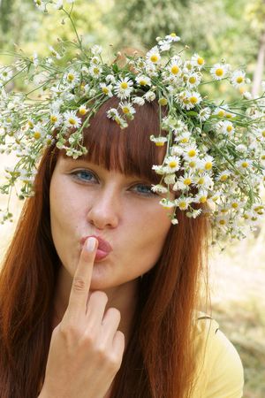 Beautiful cheerful girl in field flower garland outdoors showing secret signの写真素材