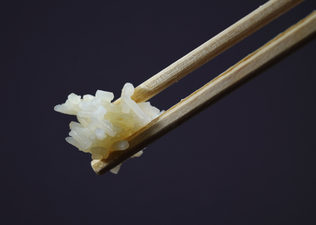 Extreme closeup (macro) of wood chopsticks holding white rice on black background - isolatedの写真素材