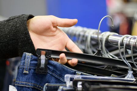 Male hand looking through pants on a clothing rack in storeの写真素材