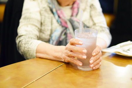Senior woman hands holding water glass at restaurantの写真素材