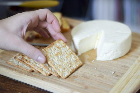 Man hand picking up a wheat cracker from a Brazilian cheese board with Minas cheeseの写真素材