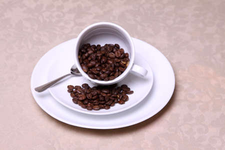 Coffee beans spilling from a cup onto a saucer.
