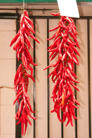 Two strings of red chilli peppers hanging outside a grocery shopの写真素材