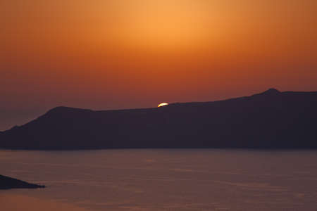 The evening sun setting behind the caldera of Santorini in the Aegean seaの写真素材