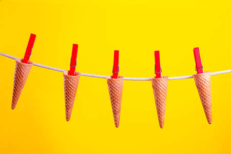 concept ice cream cones hanging by a thread with red clothespins on a vibrant yellow background