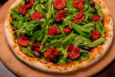 Arugula and sun dried tomato pizza on wooden board and vegetables in the background.の写真素材