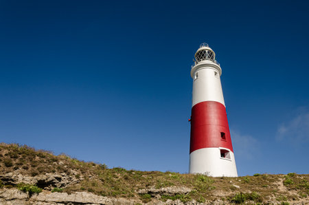 Portland Bill lighthouse at the top of the cliffs against a clear blue sky, Portland, Dorset, UKの写真素材