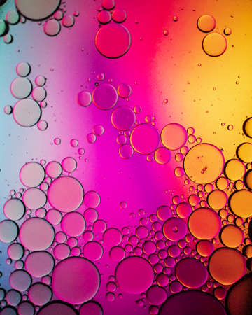 Oil drops on a water surface abstract with a bright yellow and pink background