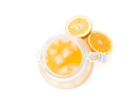 Freshly squeezed orange juice with ice cubes insice a glass jug that's accompanied by two freshly cut orange halves.の写真素材