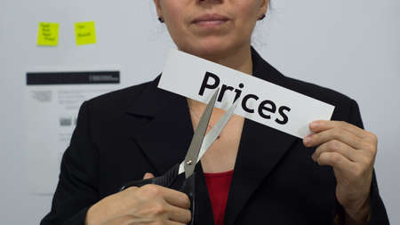 Female office worker or business woman cuts a piece of paper with the word prices on it as a price reduction business concept.の写真素材