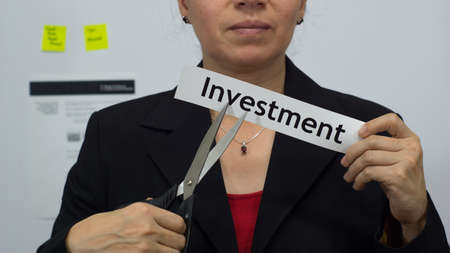 Female office worker or business woman cuts a piece of paper with the word investment on it as an investment reduction business concept.の写真素材
