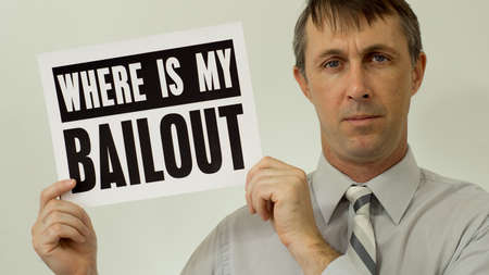 Middle aged man wearing a dress shirt and tie holds up a sign that asks where his bailout is which refers to his financial situation and bankruptcy.の写真素材