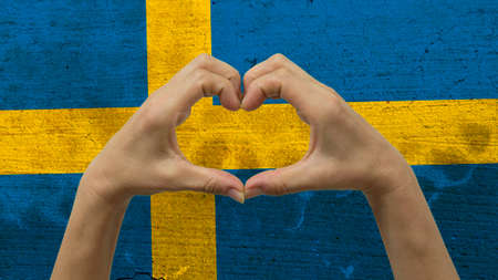 With a stylized Swedish flag background an anonymous person's hands being held in the form of a heart, symbolizing love and patriotism for Sweden.の写真素材