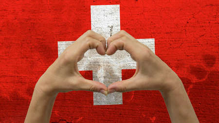 With a stylized Swiss flag background an anonymous person's hands being held in the form of a heart, symbolizing love and patriotism for Switzerland.の写真素材