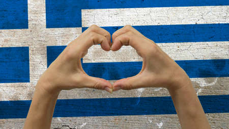 With a stylized Greek flag background an anonymous person's hands being held in the form of a heart, symbolizing love and patriotism for Greece.の写真素材