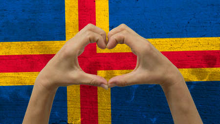 With a stylized Alandic flag background an anonymous person's hands being held in the form of a heart, symbolizing love and patriotism for Aland Islands.の写真素材