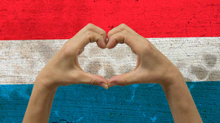 With a stylized Luxembourgish flag background an anonymous person's hands being held in the form of a heart, symbolizing love and patriotism for Luxembourg.の写真素材