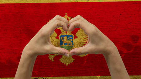 With a stylized Montenegro flag background an anonymous person's hands being held in the form of a heart, symbolizing love and patriotism for Montenegro.の写真素材