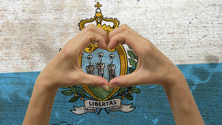 With a stylized San Marino flag background an anonymous person's hands being held in the form of a heart, symbolizing love and patriotism for San Marino.の写真素材
