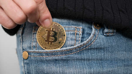 Close up shot of a woman putting a Bitcoin cryptocurrency coin into her front jeans pocket.の写真素材