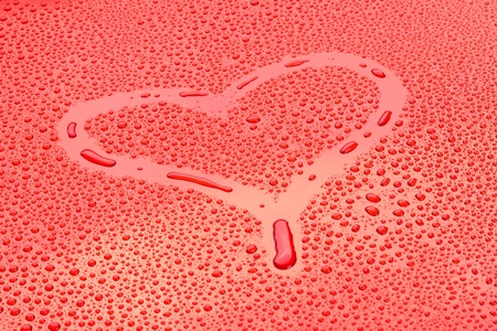 heart drawn in drops o water on red backgroundの写真素材