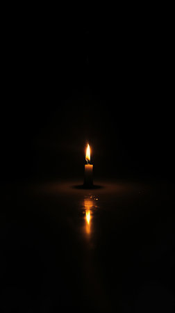 Lit candle in darkness with reflection on glossy surface, serene and contemplative atmosphere conceptの素材