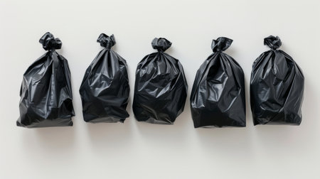 Five black garbage bags lined up on a white background, household waste disposal conceptの素材