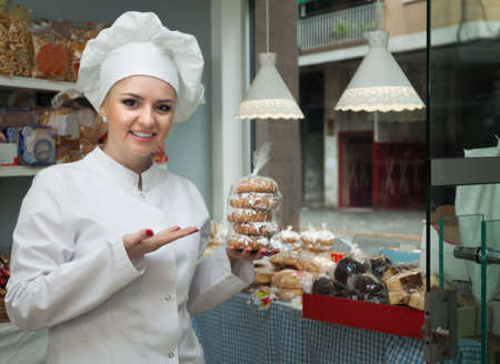 Portrait of beautiful young chef at confectionery display with pastry