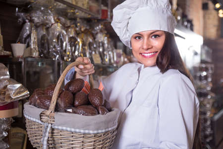 Young shopgirl posing with fine chocolate eggs and cakes in shopの写真素材