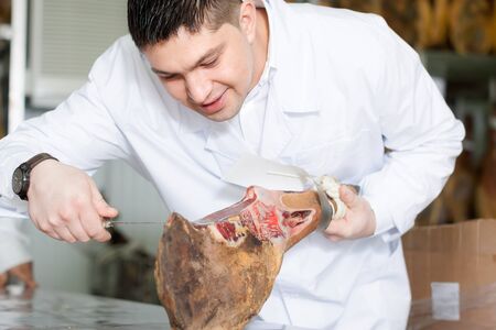 Midle aged butcher cuts sausages and jamon in delicatessen storeの写真素材